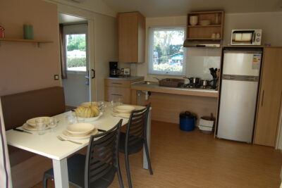 Salle à manger et cuisine du mobil-home Optiméo. La table est dressée pour 4 personnes. - Agrandir l'image 2 sur 8, fenêtre modale